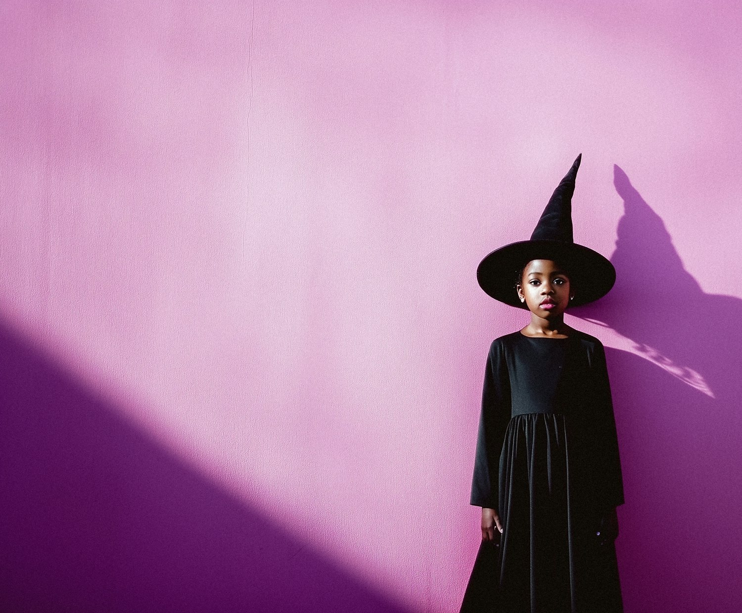 Young Girl in Witch Costume Against Pink Background