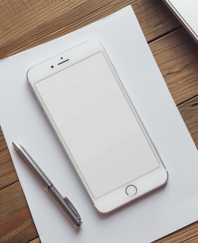 Modern Smartphone with Pen and Paper on Wooden Desk