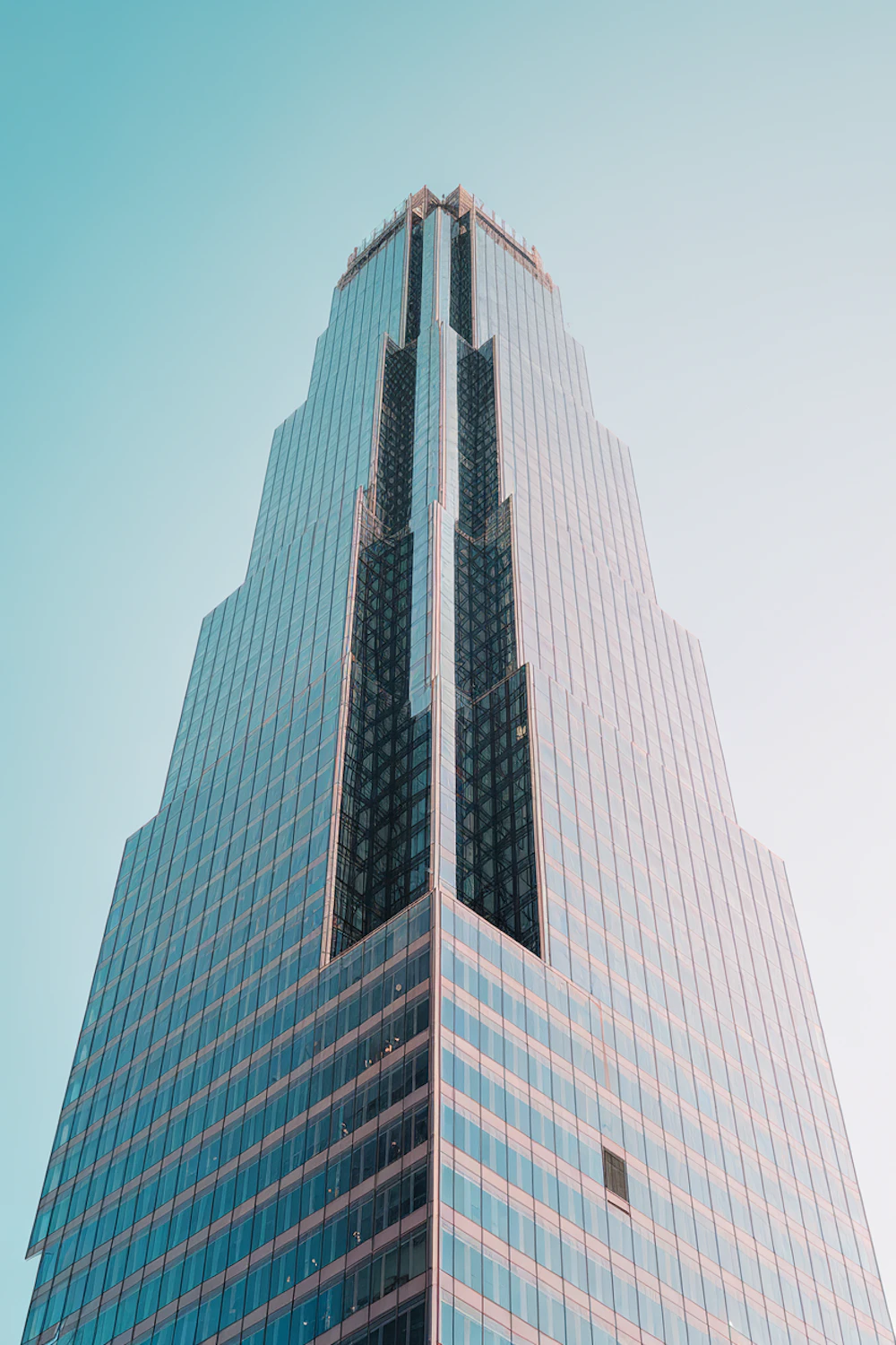 A sleek skyscraper with a glass facade reflecting a blue sky
